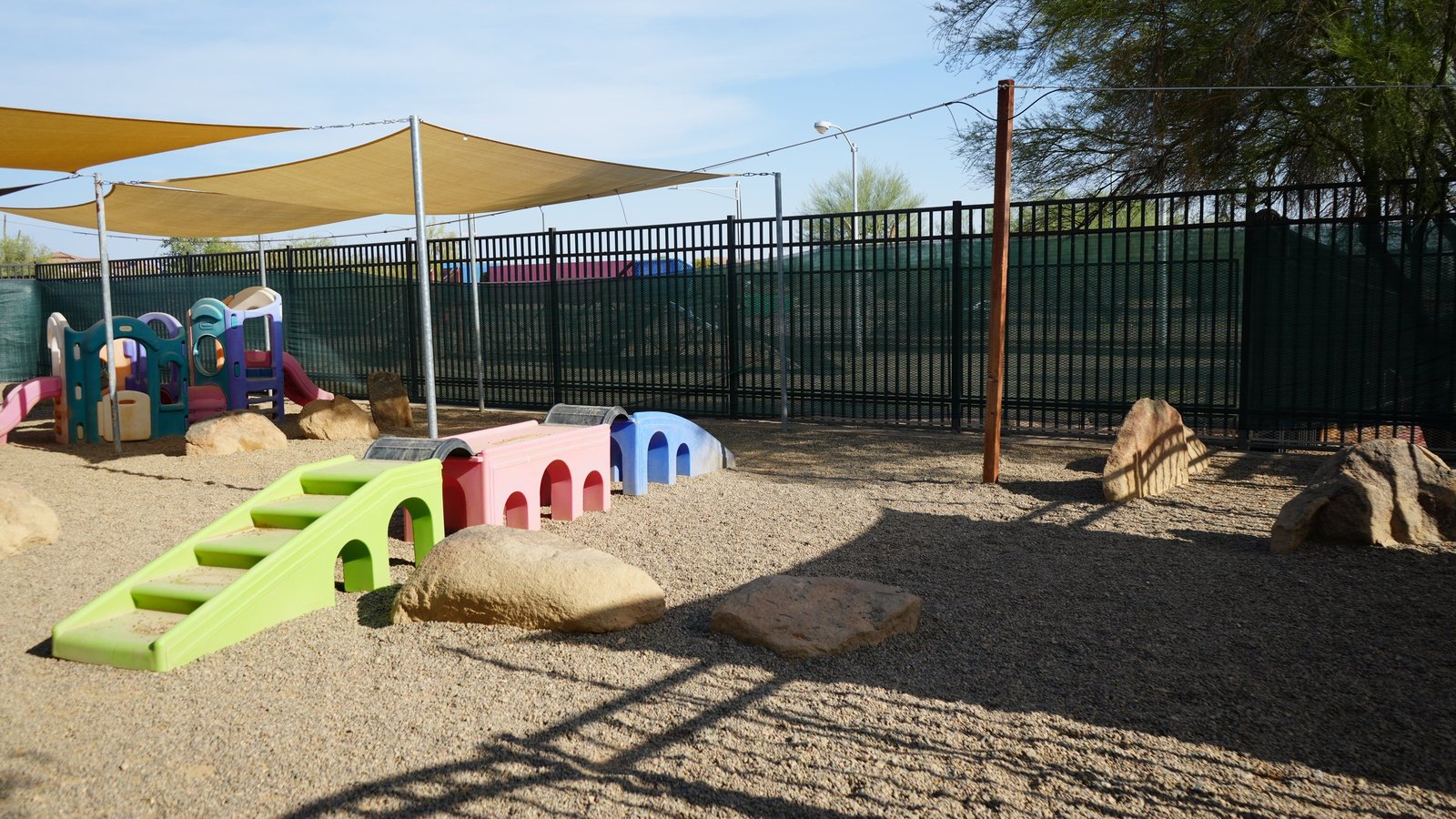 An outdoor yard at Cave Creek with pastel dog houses, gravel and shade in the desert.