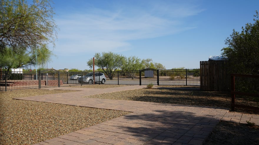 The Cave Creek desert entrance with paver walkways leading to a metal driveway gate, open high-desert land beyond.