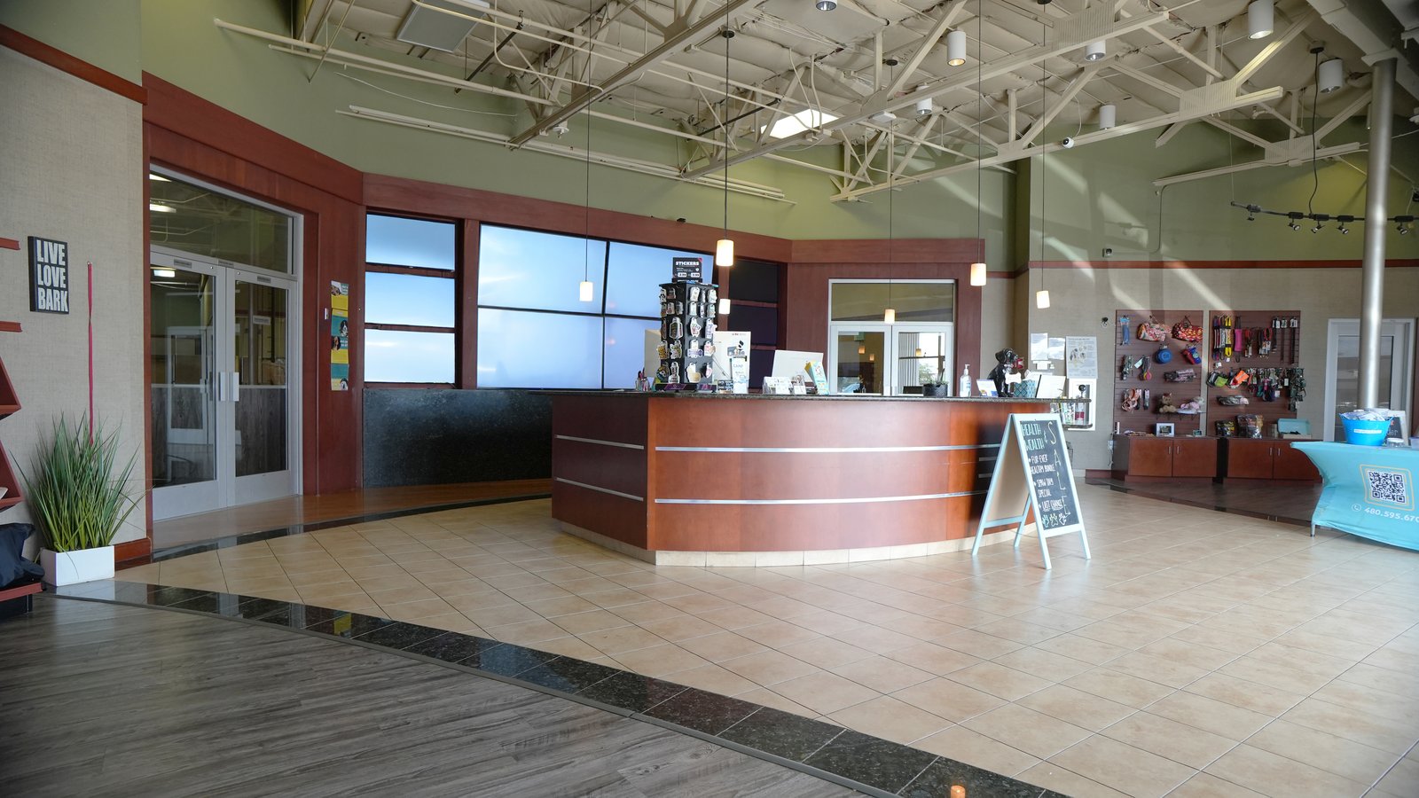 The bright, welcoming front lobby and curved wood reception desk at the Partners Dogs Scottsdale campus, with Live Love Day wall art and clean tile floors.