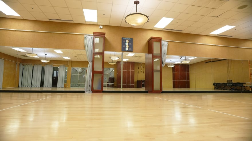 A bright, empty climate-controlled indoor training room with a wall mirror and polished wood floor at the Scottsdale campus.