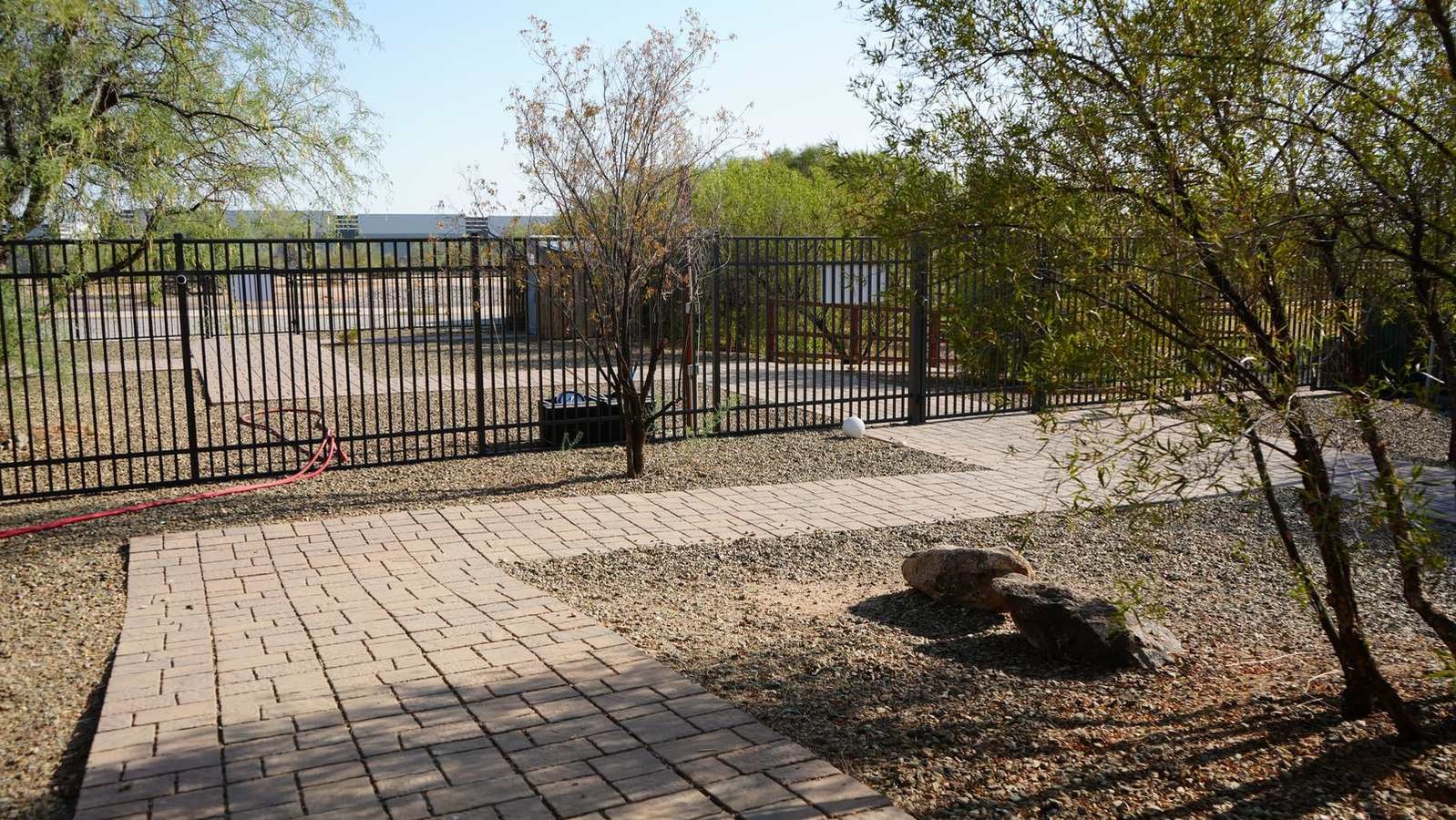 A paver walkway at the Cave Creek campus leads through desert landscaping to a metal gate, with facility buildings beyond.