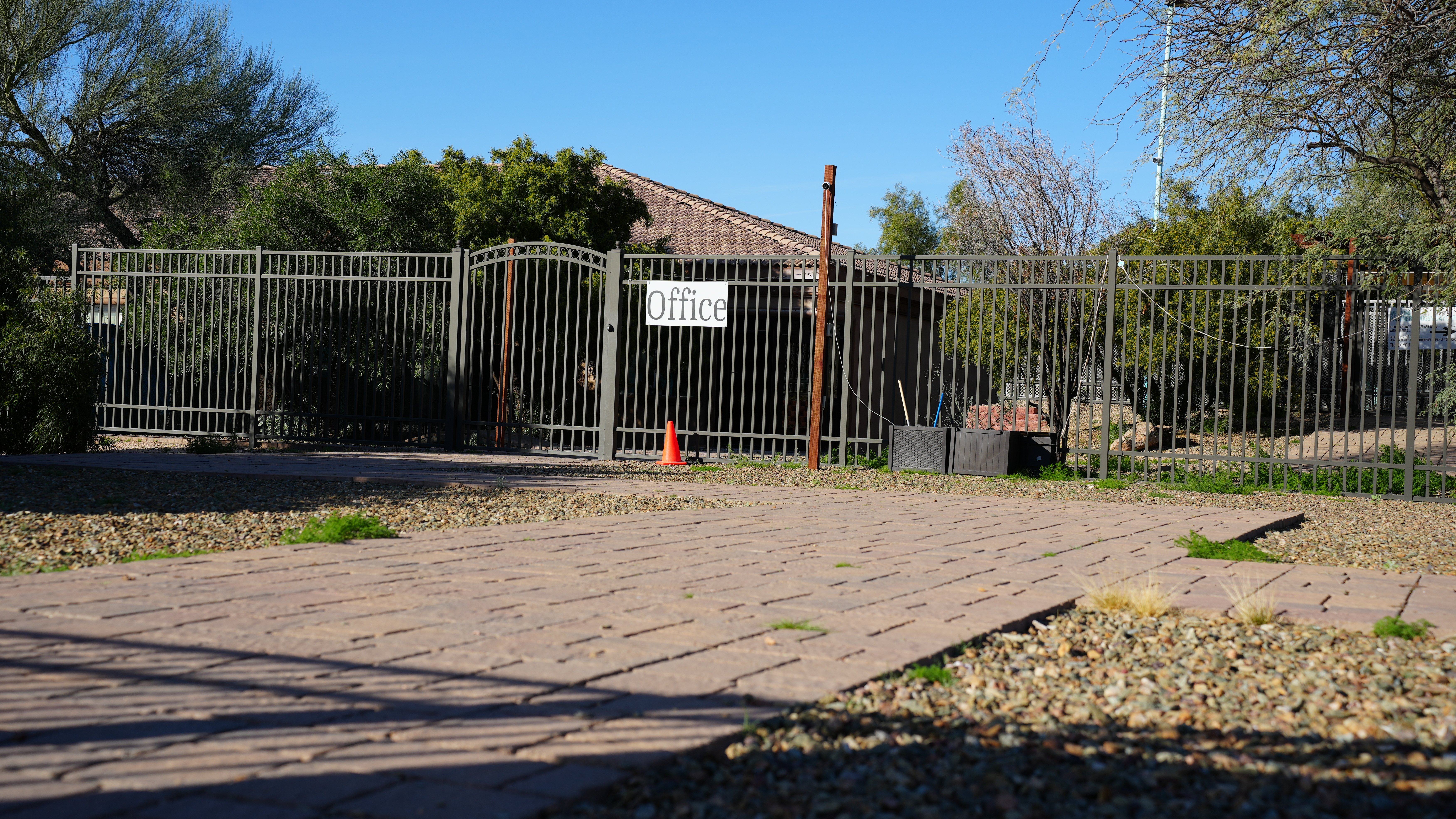 The wrought-iron entrance gate at the Cave Creek campus with an Office sign, set behind a paver driveway under a clear desert sky.